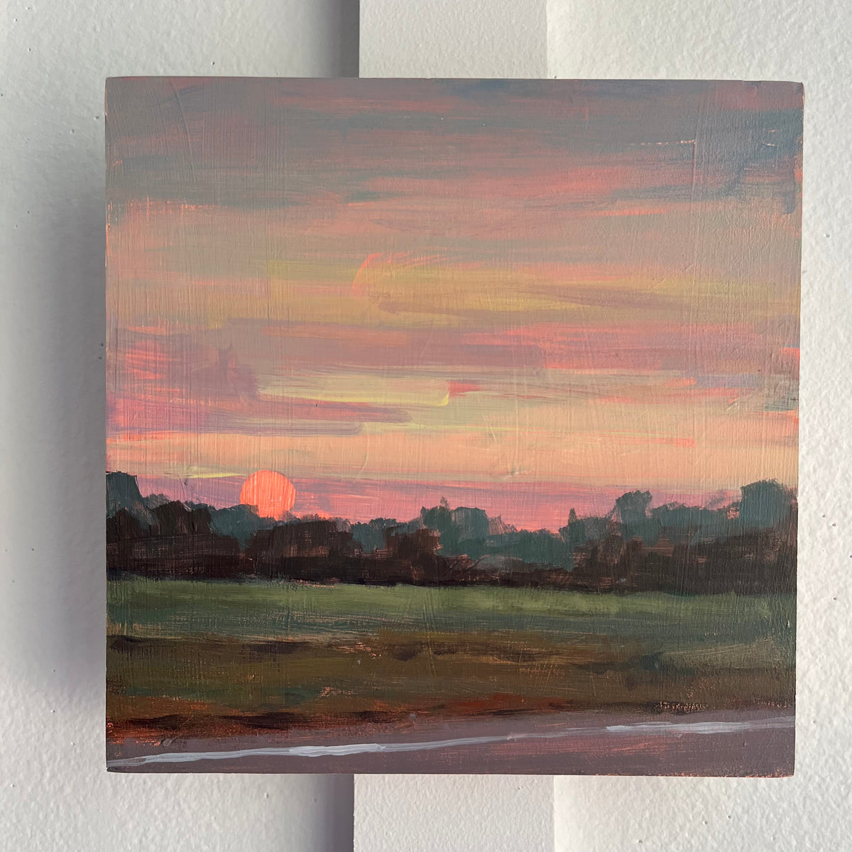 The Long Way Home — a pink and orange sunset above a dark tree line and marsh. Painting by Maggie Stickney.