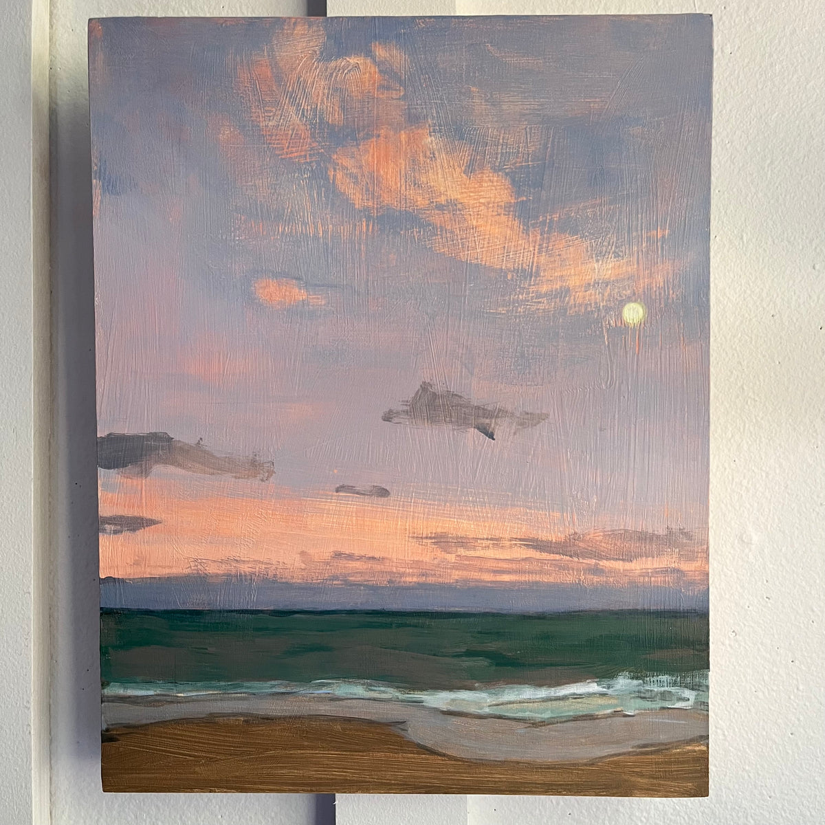 Atlantic Moonrise — a small moon and peach clouds above blue-green waves and a sandy beach. Painting by Maggie Stickney.
