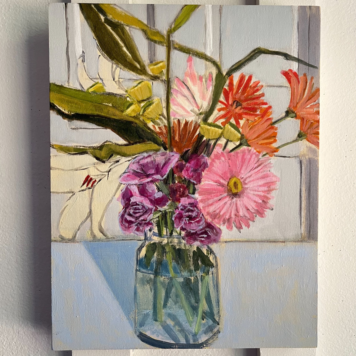 Kitchen Counter — pink, purple, and orange flowers with broad leaves in a blue-green glass jar. Painting by Maggie Stickney.
