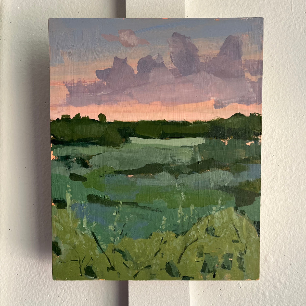 Green Before Dark — green marsh grasses and waterways beneath purple clouds and a pink horizon. Painting by Maggie Stickney.