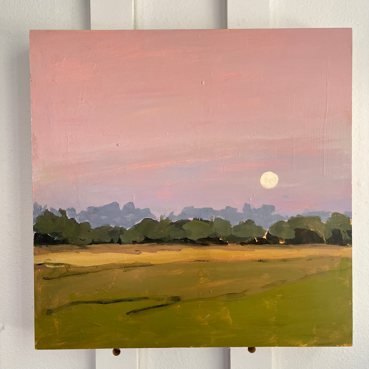 Summer Night — a full moon in a pink sky above a golden field and dark tree line. Painting by Maggie Stickney.