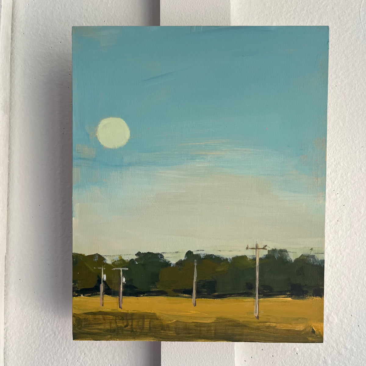 Super Moon — a pale full moon above a yellow field and dark trees under a turquoise sky. Painting by Maggie Stickney.