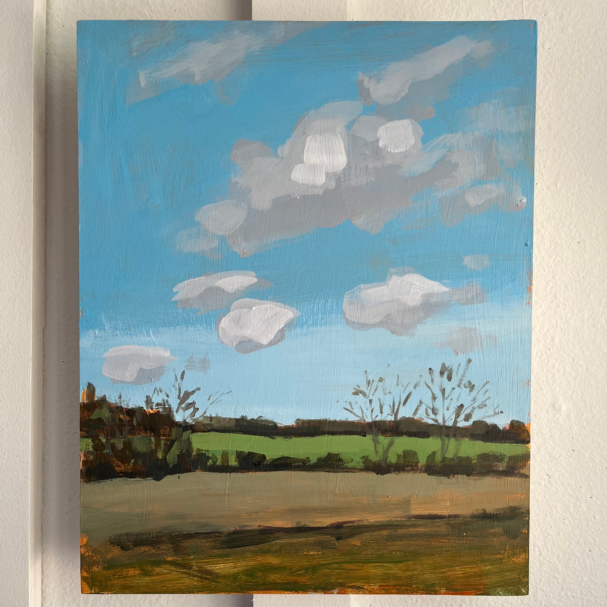 November Drive — open fields and bare trees beneath a bright blue sky with white clouds. Painting by Maggie Stickney.