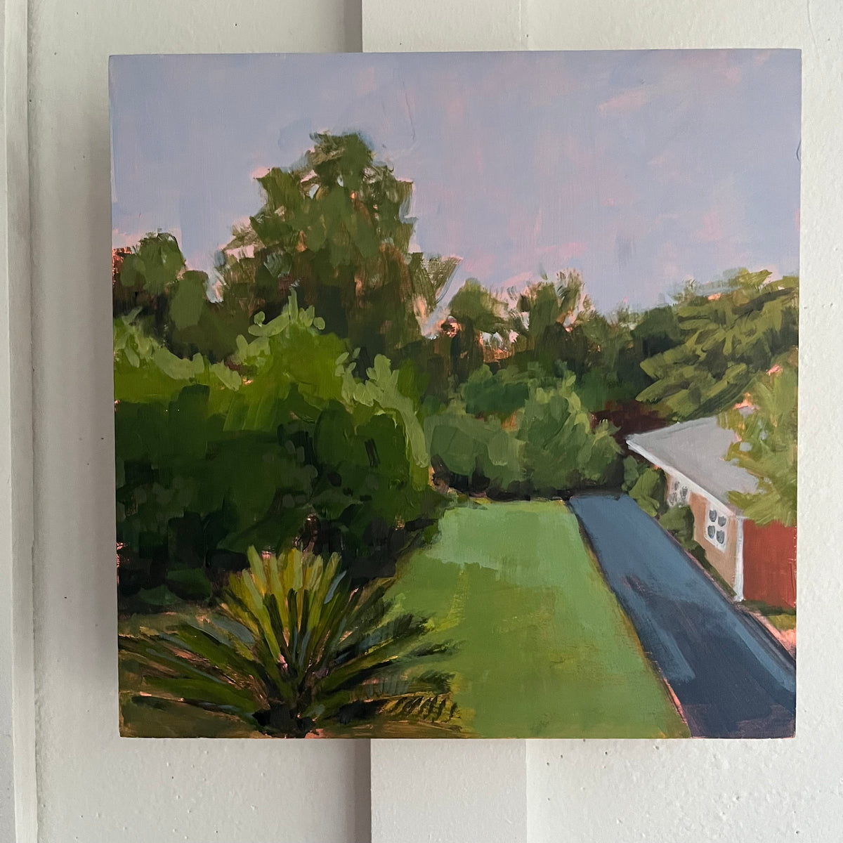 Sago Palm — a sago palm and green lawn beside a driveway and house under a lavender sky. Painting by Maggie Stickney.