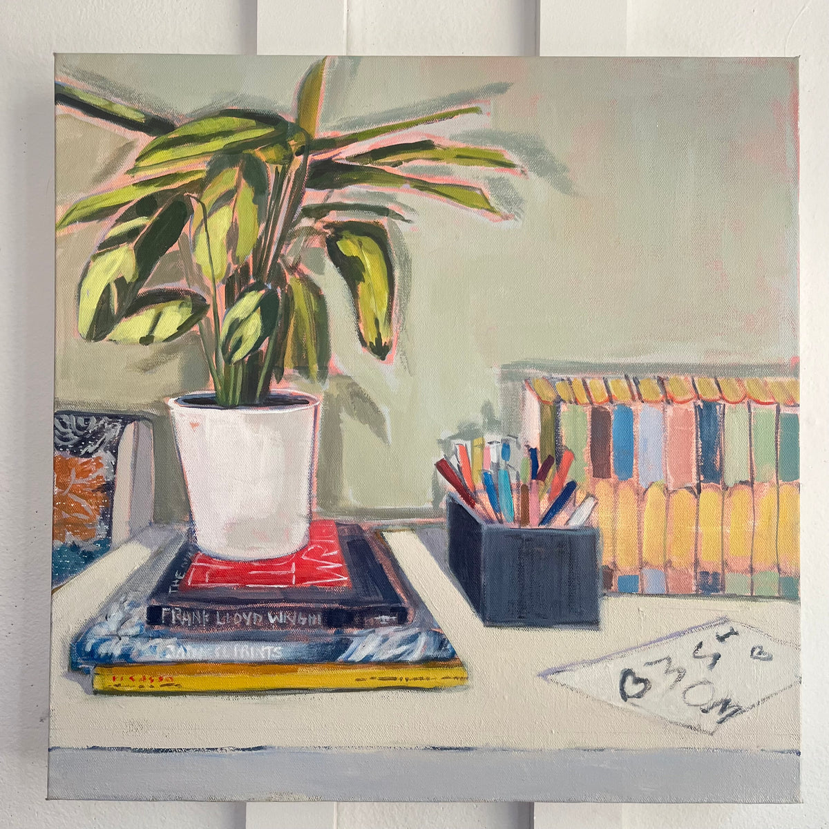 Still Life with Love Note — a potted plant on stacked books beside pencils, colorful books, and a handwritten love note. Painting by Maggie Stickney.