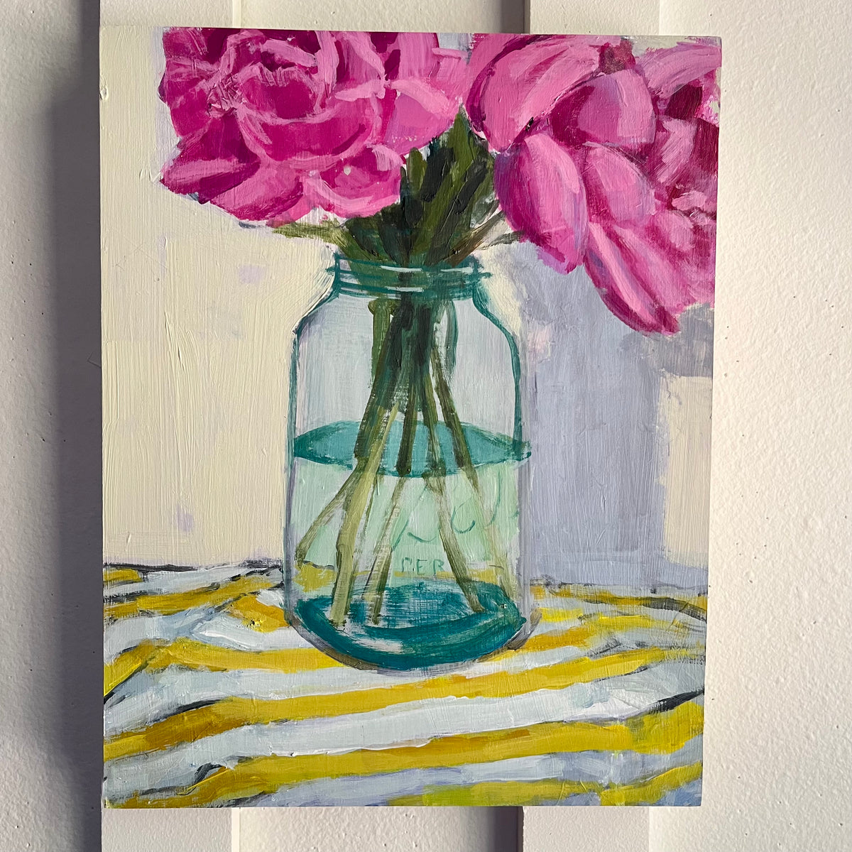 Peonies — deep pink peonies in a green glass jar on a yellow-and-white striped cloth. Painting by Maggie Stickney.