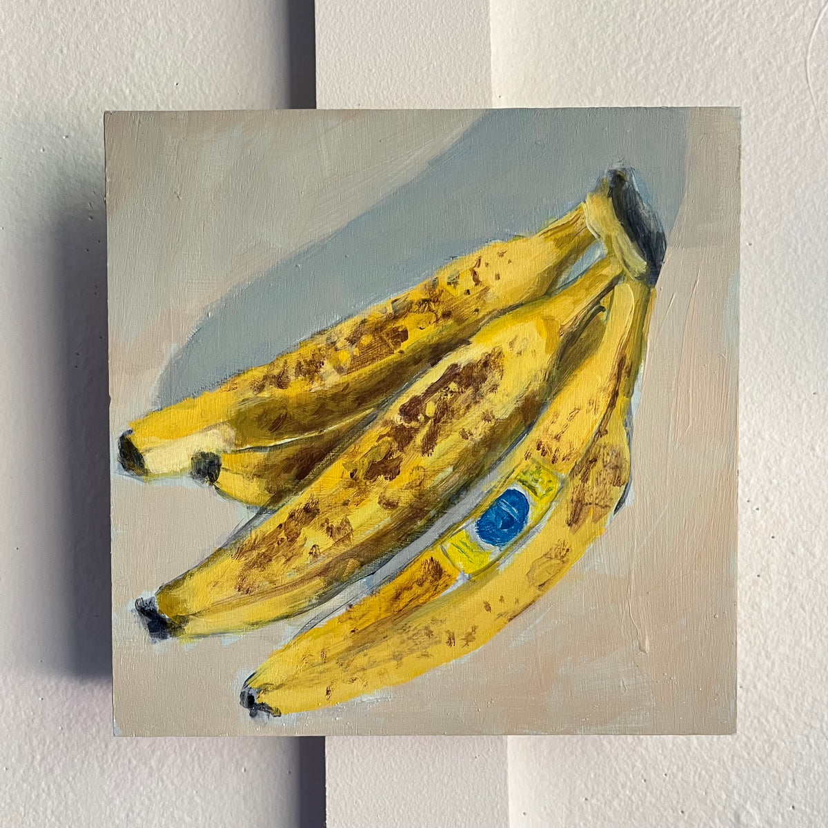 Bananas no 4 — a bunch of ripe yellow bananas with brown speckles casting a soft shadow. Painting by Maggie Stickney.
