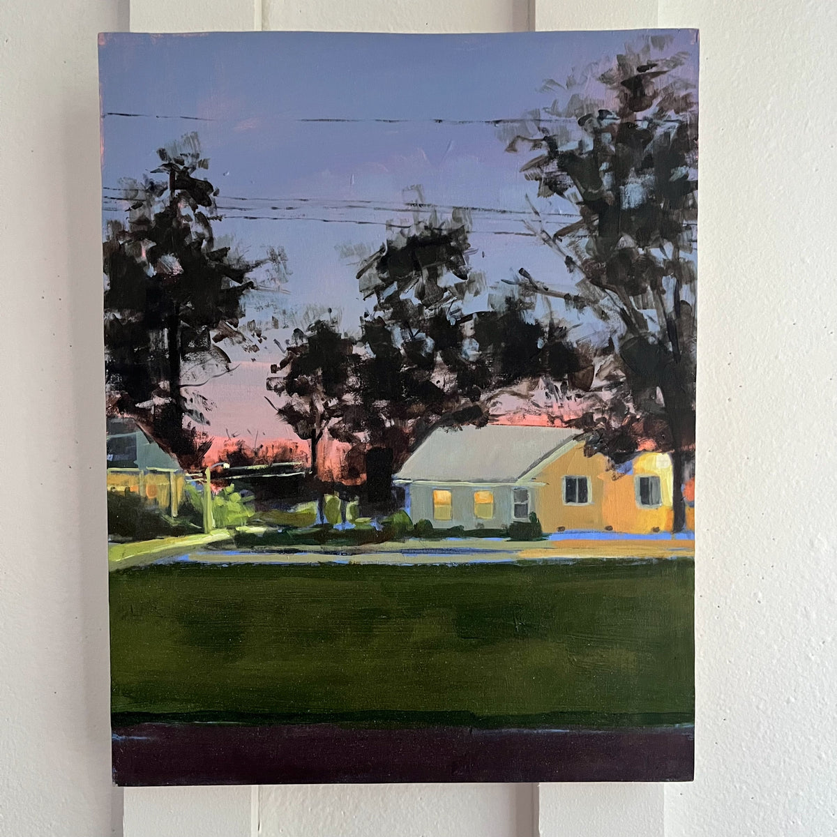 Evening Dog Walk — yellow houses and silhouetted trees beneath a lavender and pink evening sky. Painting by Maggie Stickney.