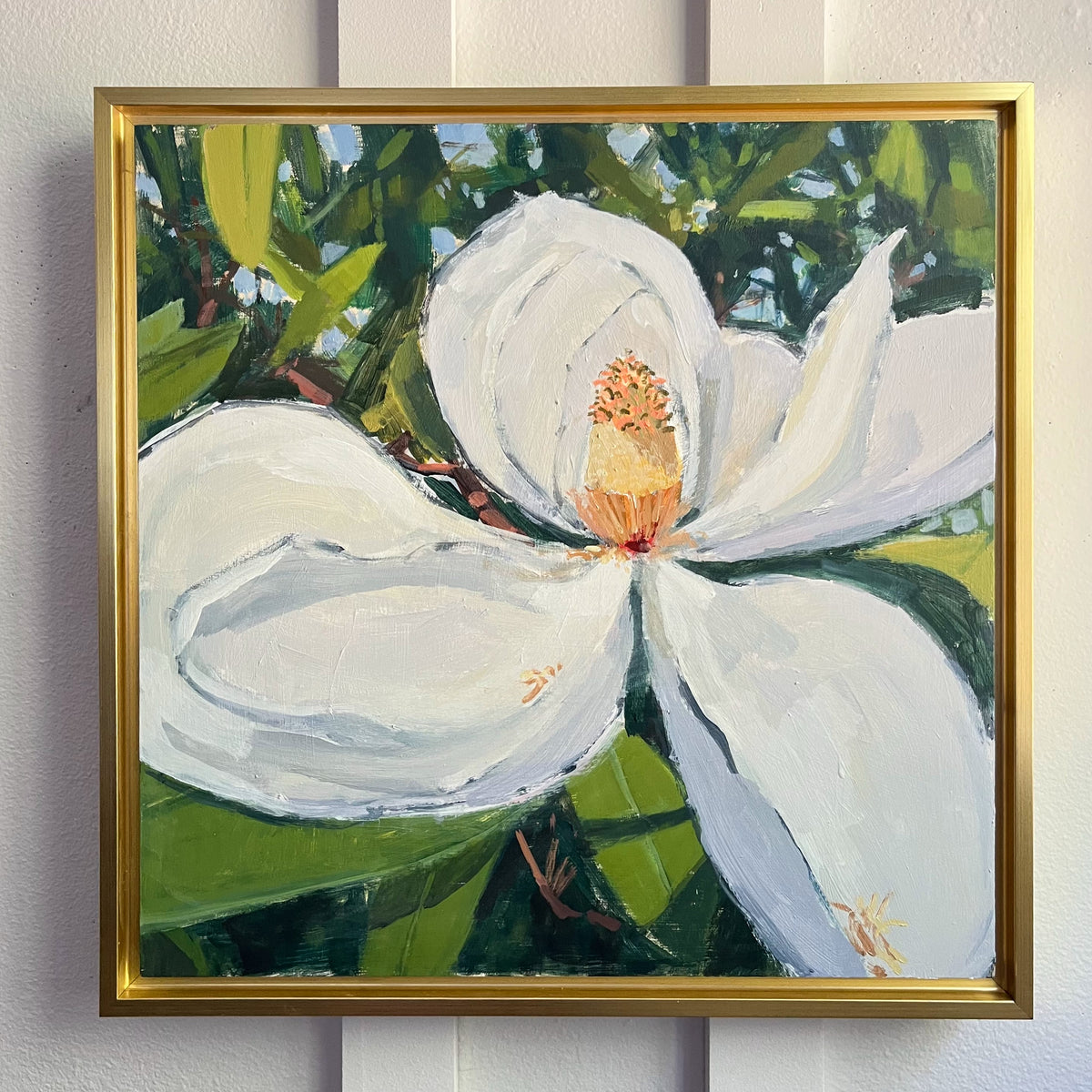 Magnolia Bloom no 2 — a large white magnolia against dark green leaves, shown in a gold-colored frame. Painting by Maggie Stickney.