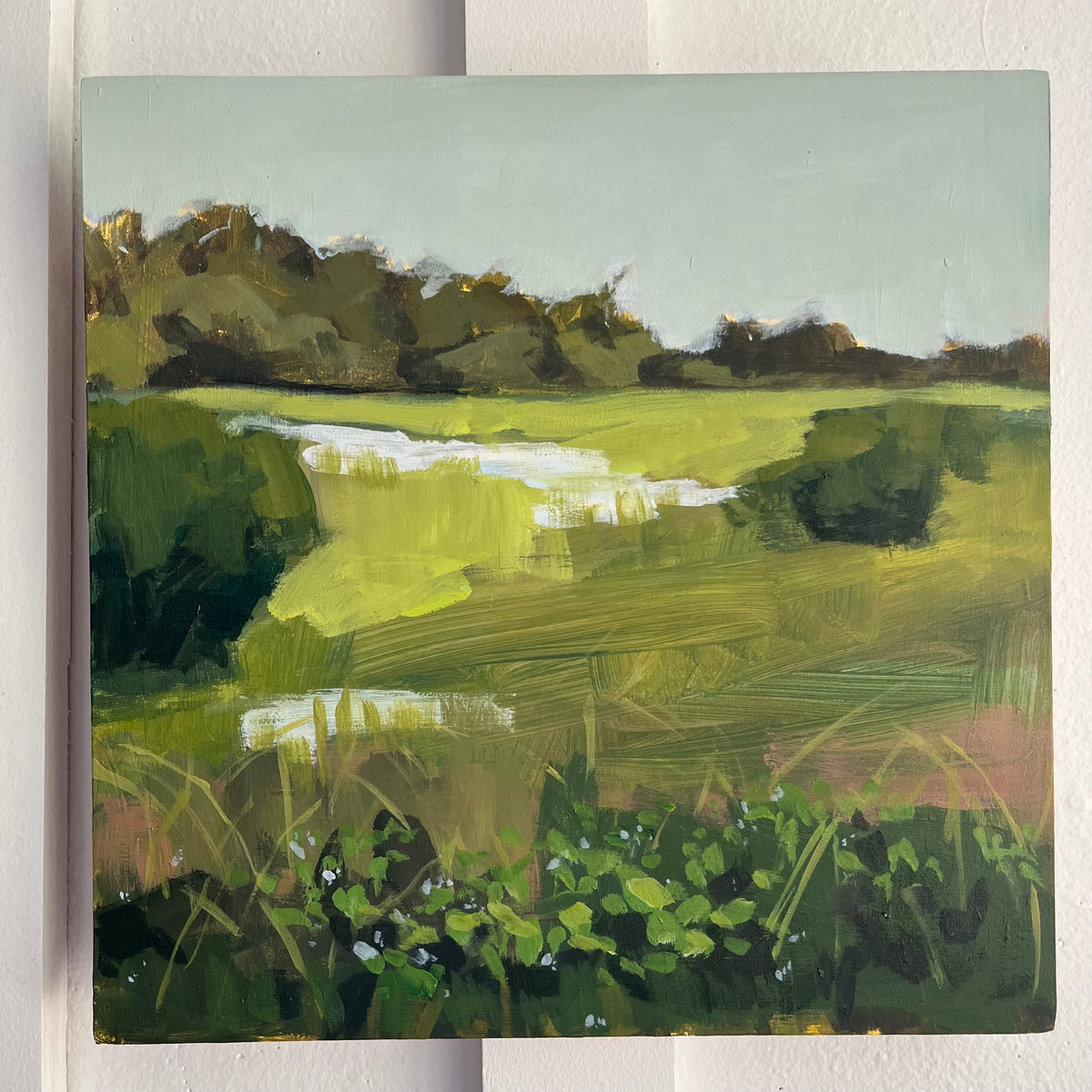Along the Way — a reflective waterway winding through bright green fields and dark trees. Painting by Maggie Stickney.