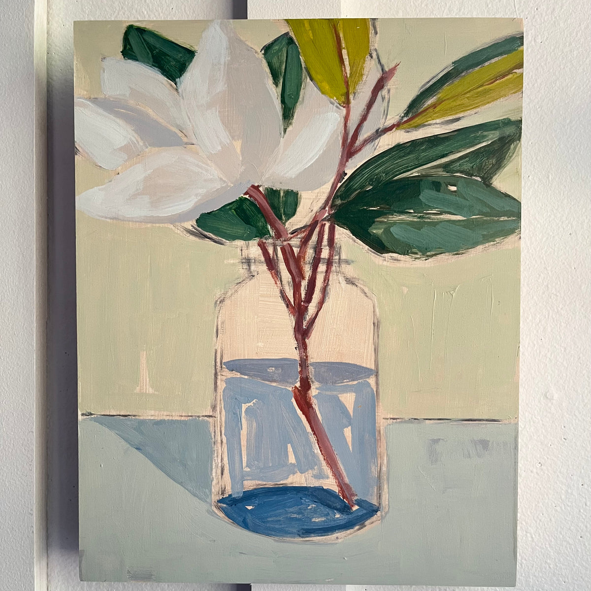 Magnolia in a Jar — a white magnolia and green leaves on a woody stem in a clear jar. Painting by Maggie Stickney.